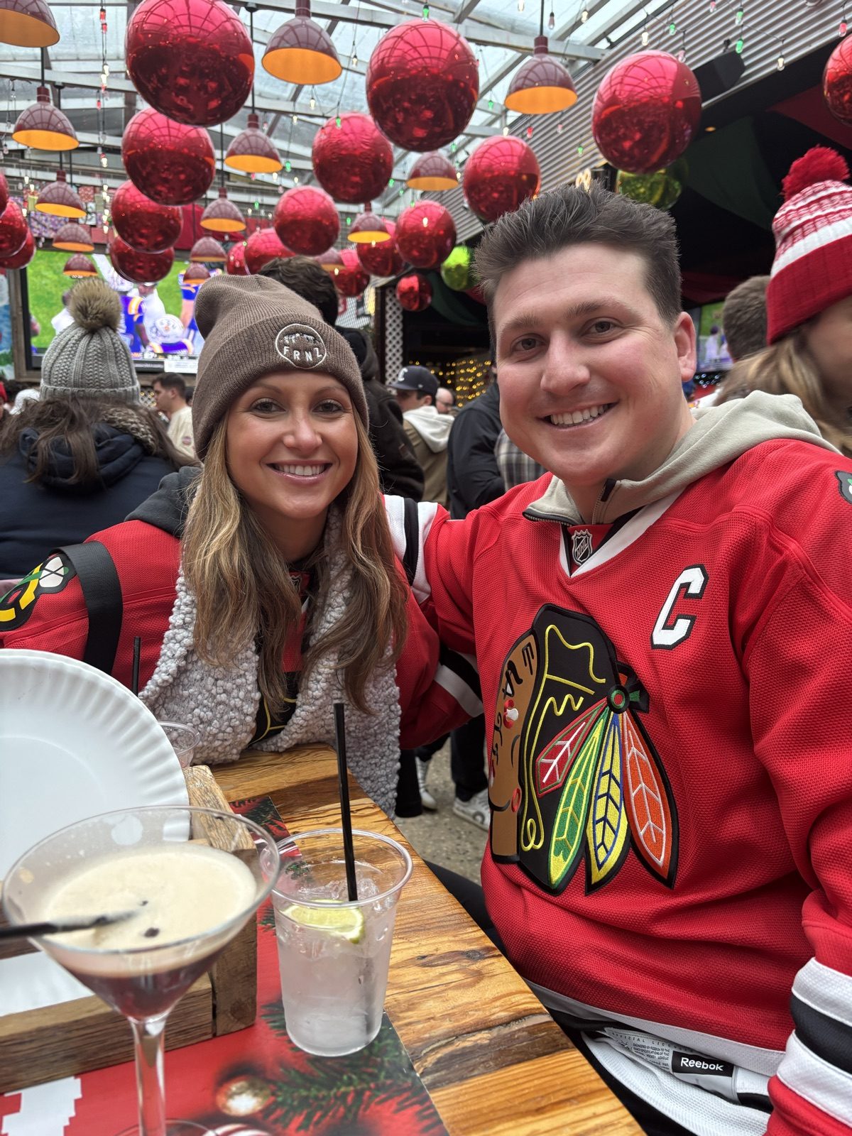 Andrew and Jenna in Blackhawks jerseys at a festive bar with ornaments overhead