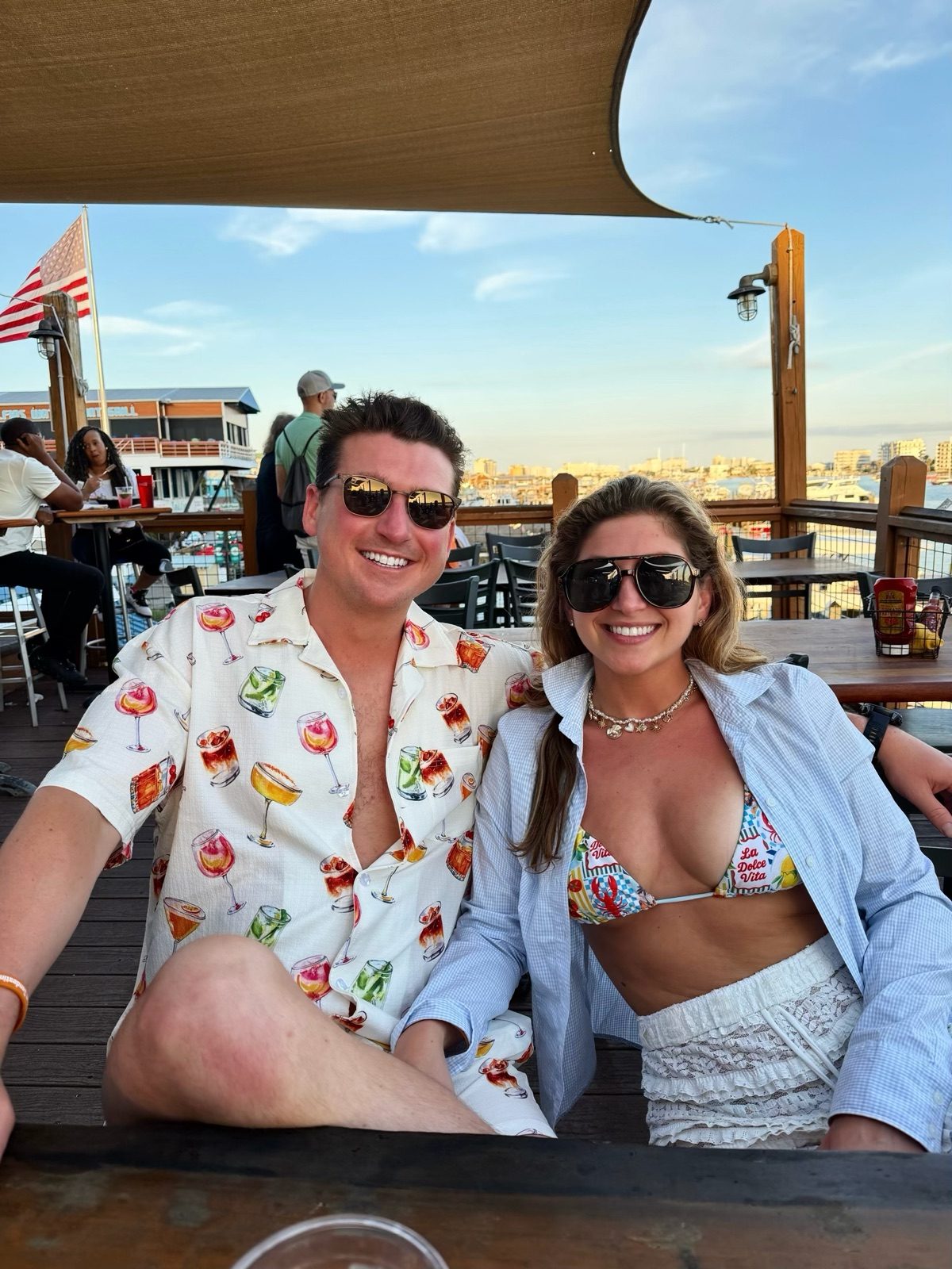 Andrew and Jenna smiling at a waterfront bar table with a harbor behind them