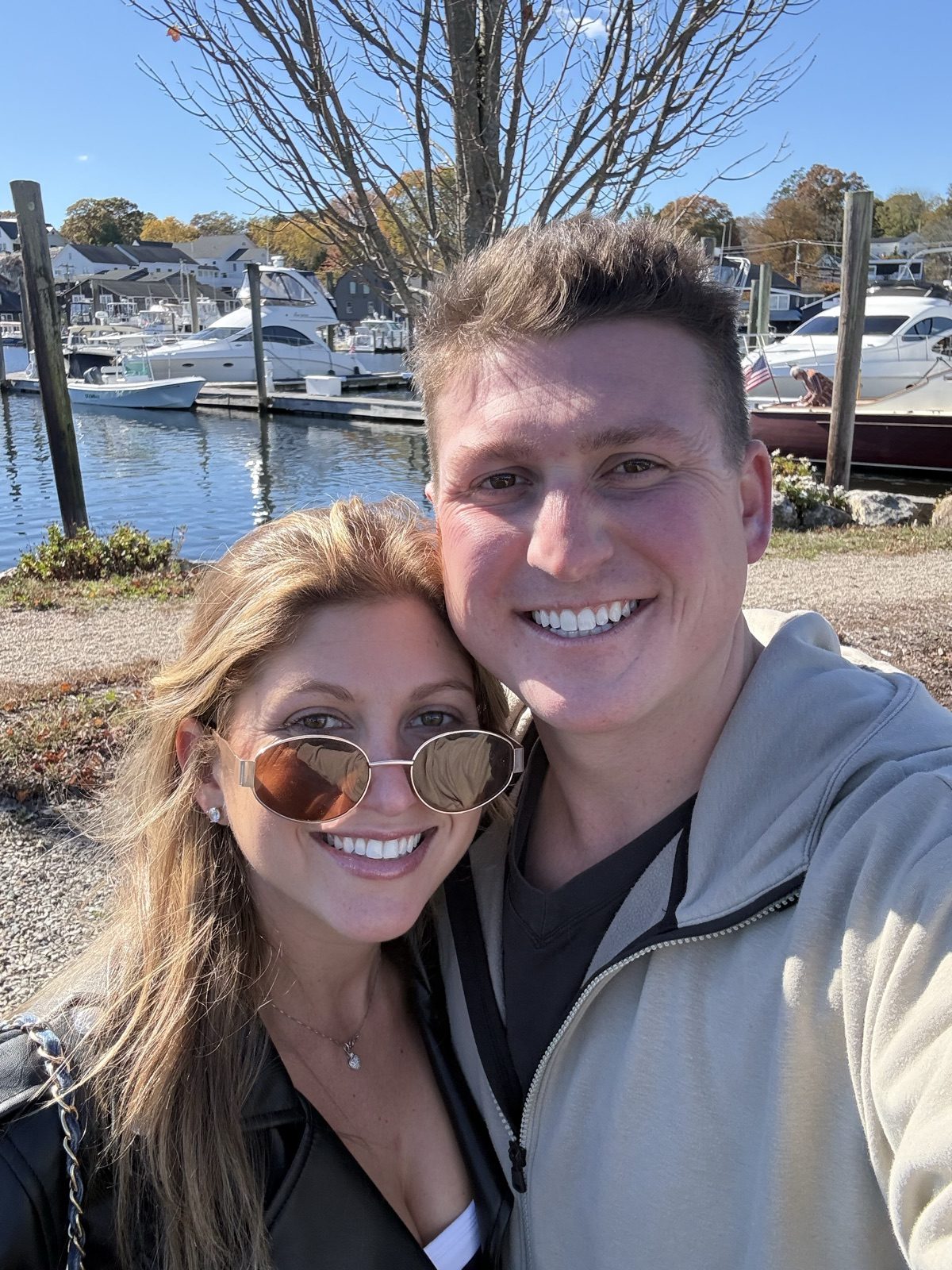 Selfie of Andrew and Jenna at a marina full of boats on a sunny fall day