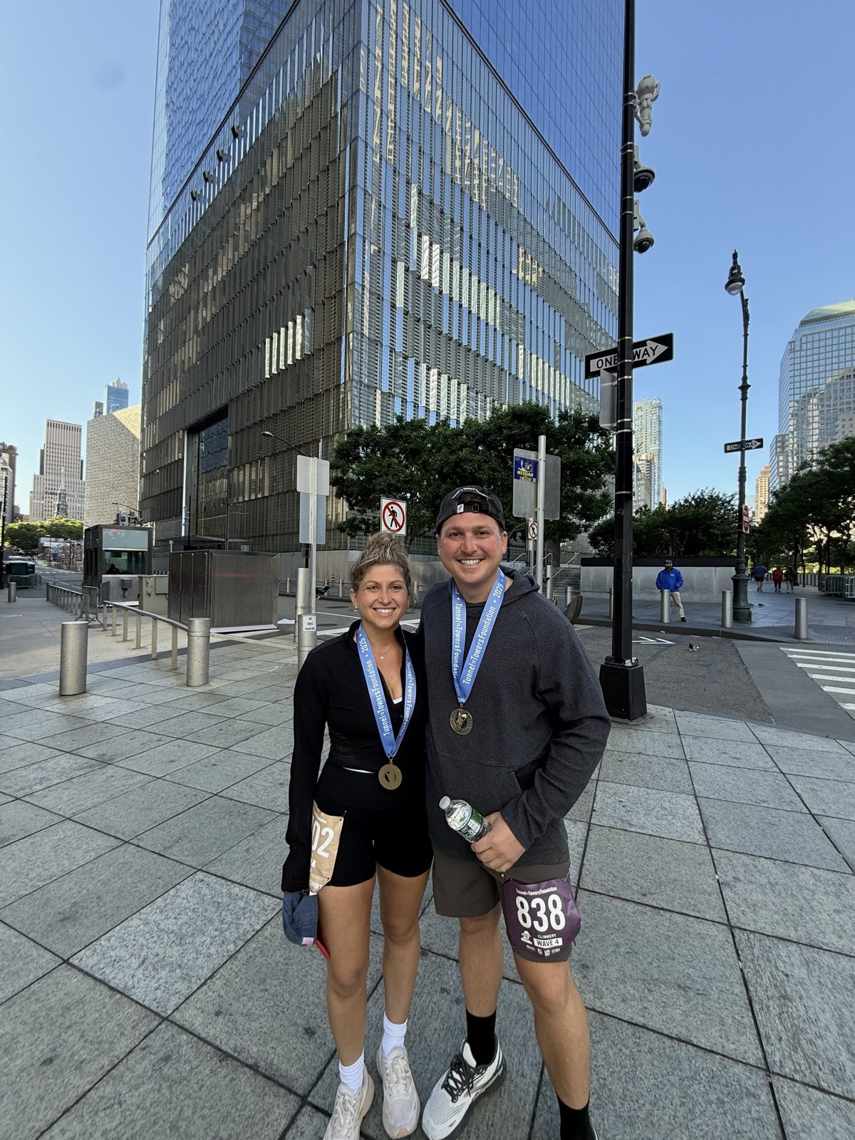 Andrew and Jenna with medals holding an 'I Climbed for Heroes' sign at One World Observatory